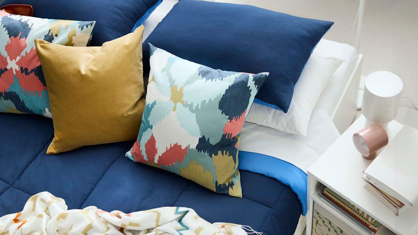 An aerial view of a bed with dark blue bed linen and colourful cushions on top.