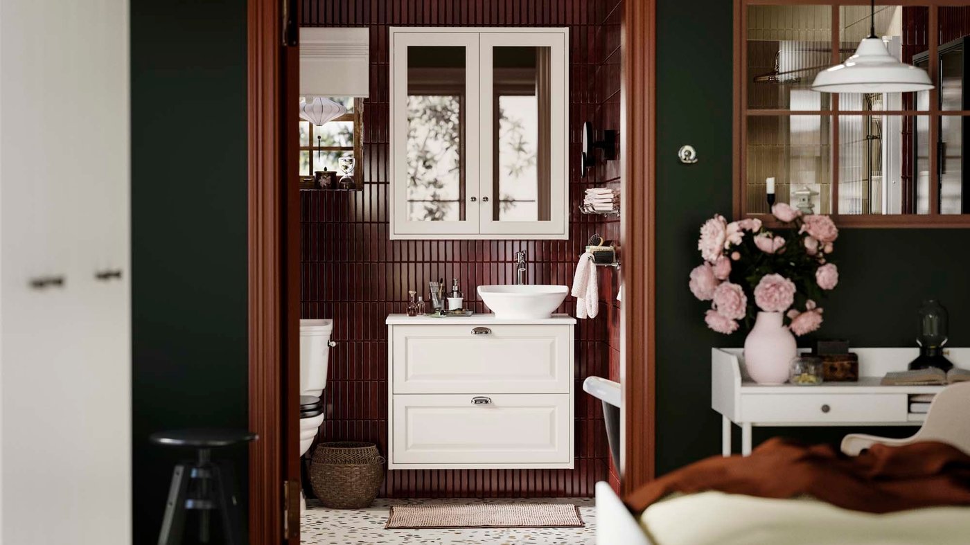 View from a bedroom of a dark coloured, tiled bathroom with white TÄNNFORSEN bathroom series in focus. 