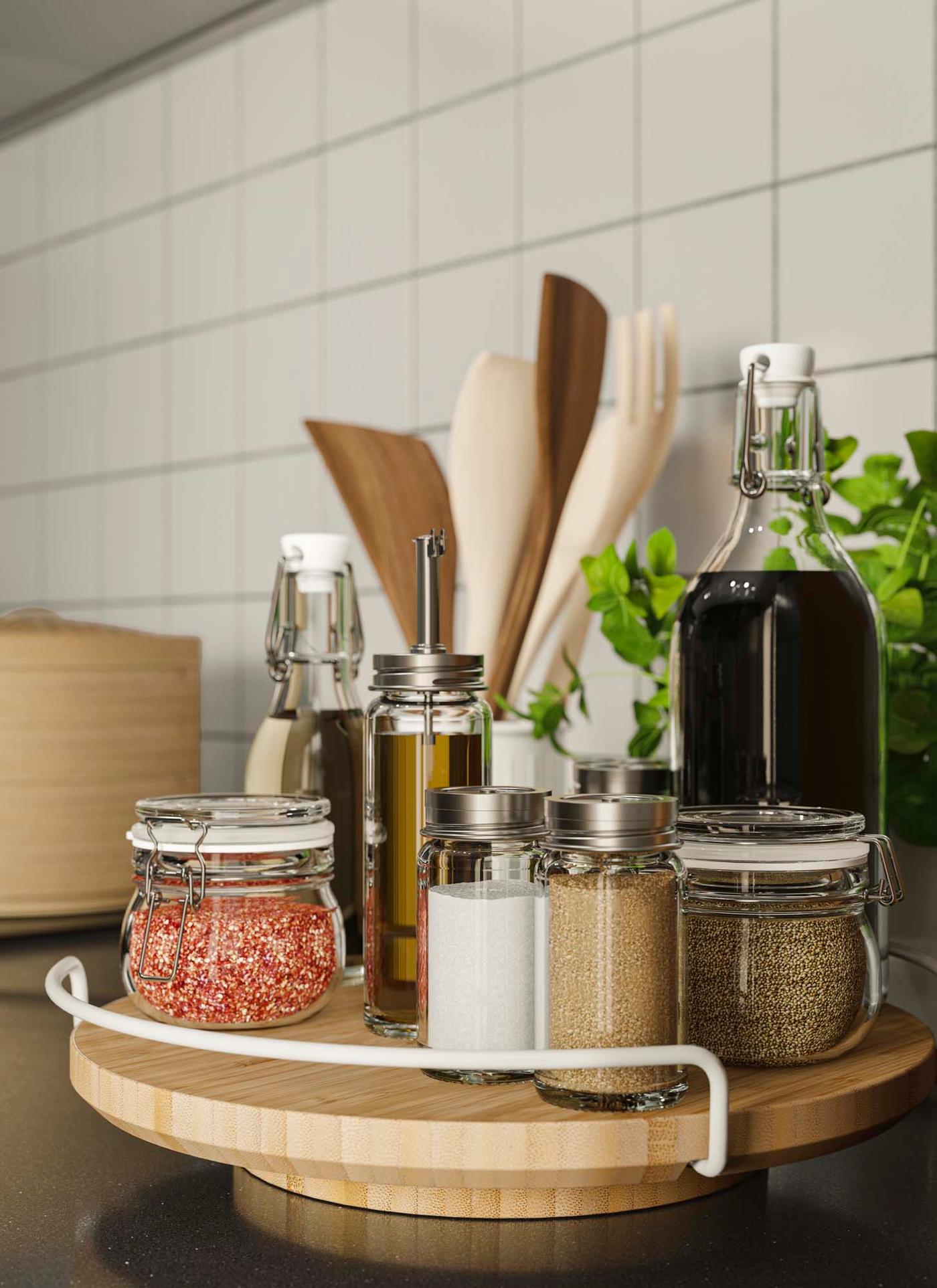 Glass jars and bottled containing olive oil, pepper and salt on a round wood lazy suzan with a white bracket.