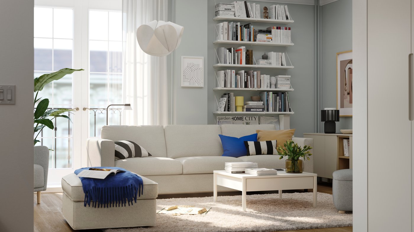 A white sofa in front of a French balcony and wall-mounted bookshelves in a living room with light blue walls. 