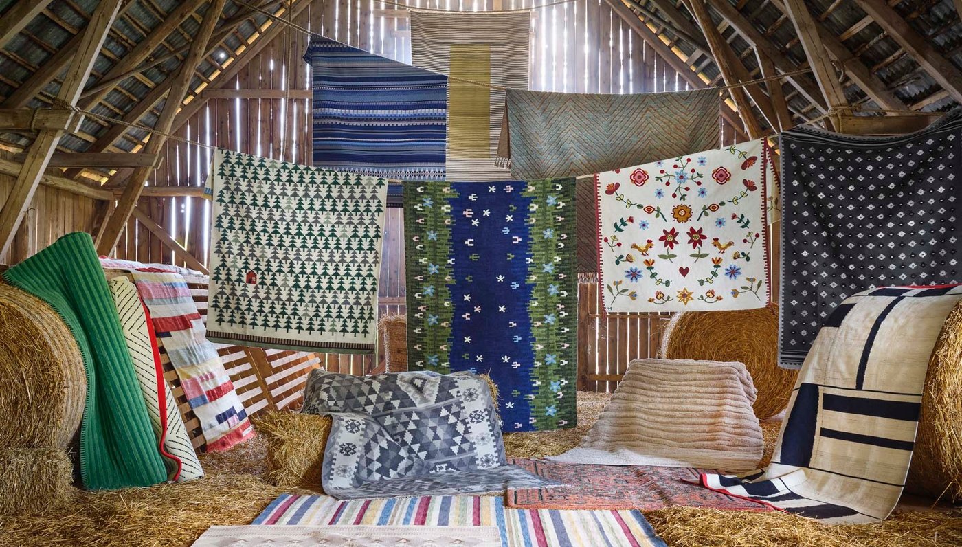 A collection of handmade rugs hanging over a line and laid out on the floor of a barn.