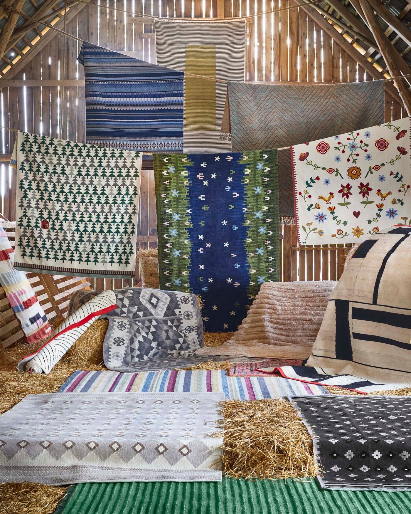 A collection of handmade rugs hanging over a line and laid out on the floor of a barn.