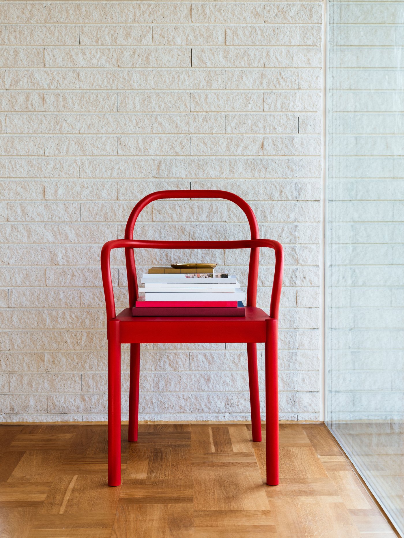 A red wooden chair with bent arches in armrest and back is standing freely on a wooden floor.