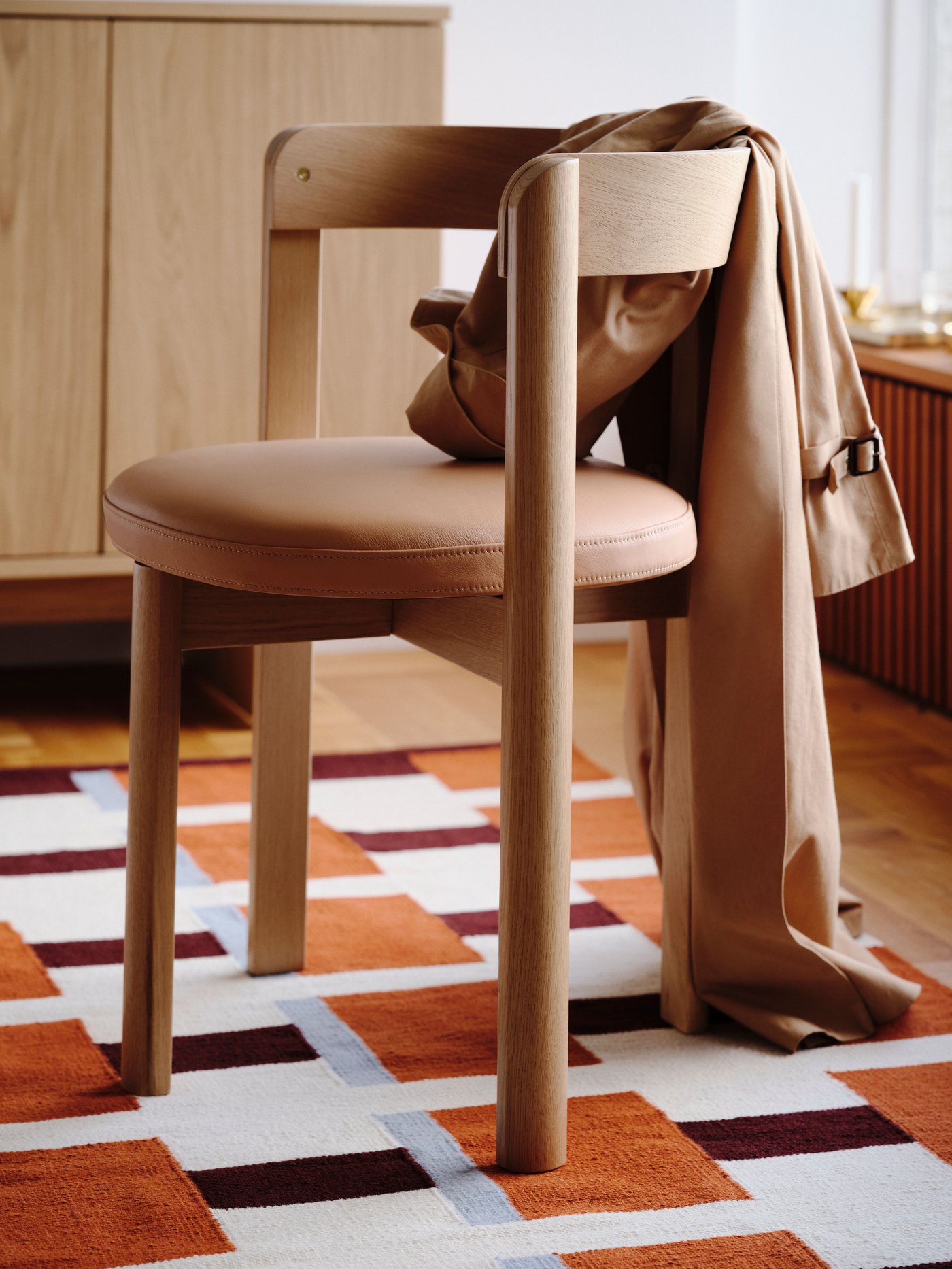Freestanding oak chair with curved back and Seglora leather cushion on an orange patterned rug, brown throw draped over the back