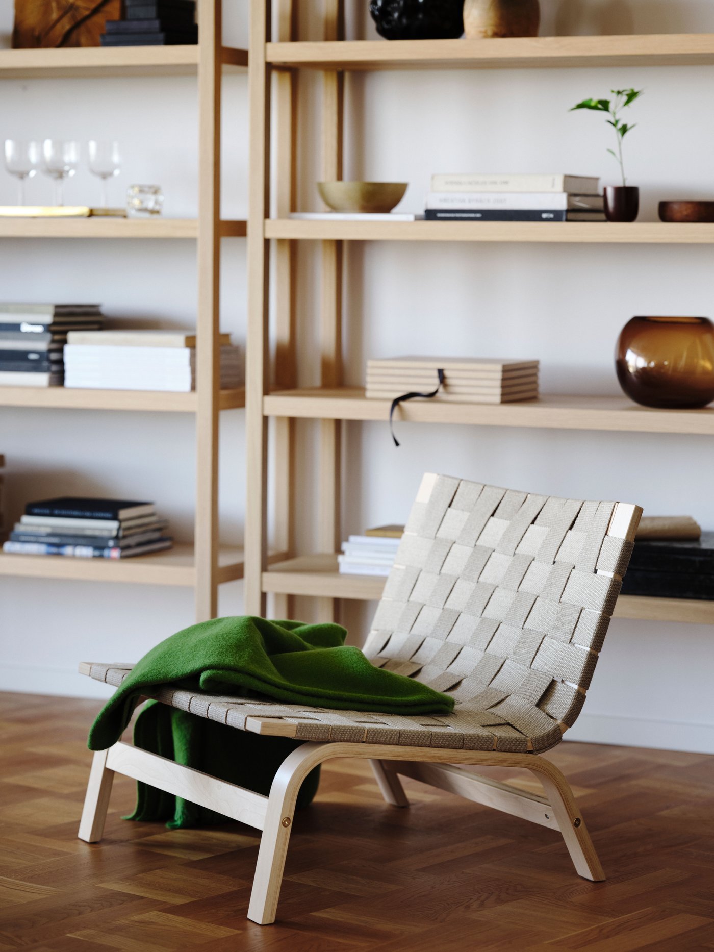 Saddle weave low chair with folded green merino throw in front of wide decorated shelves