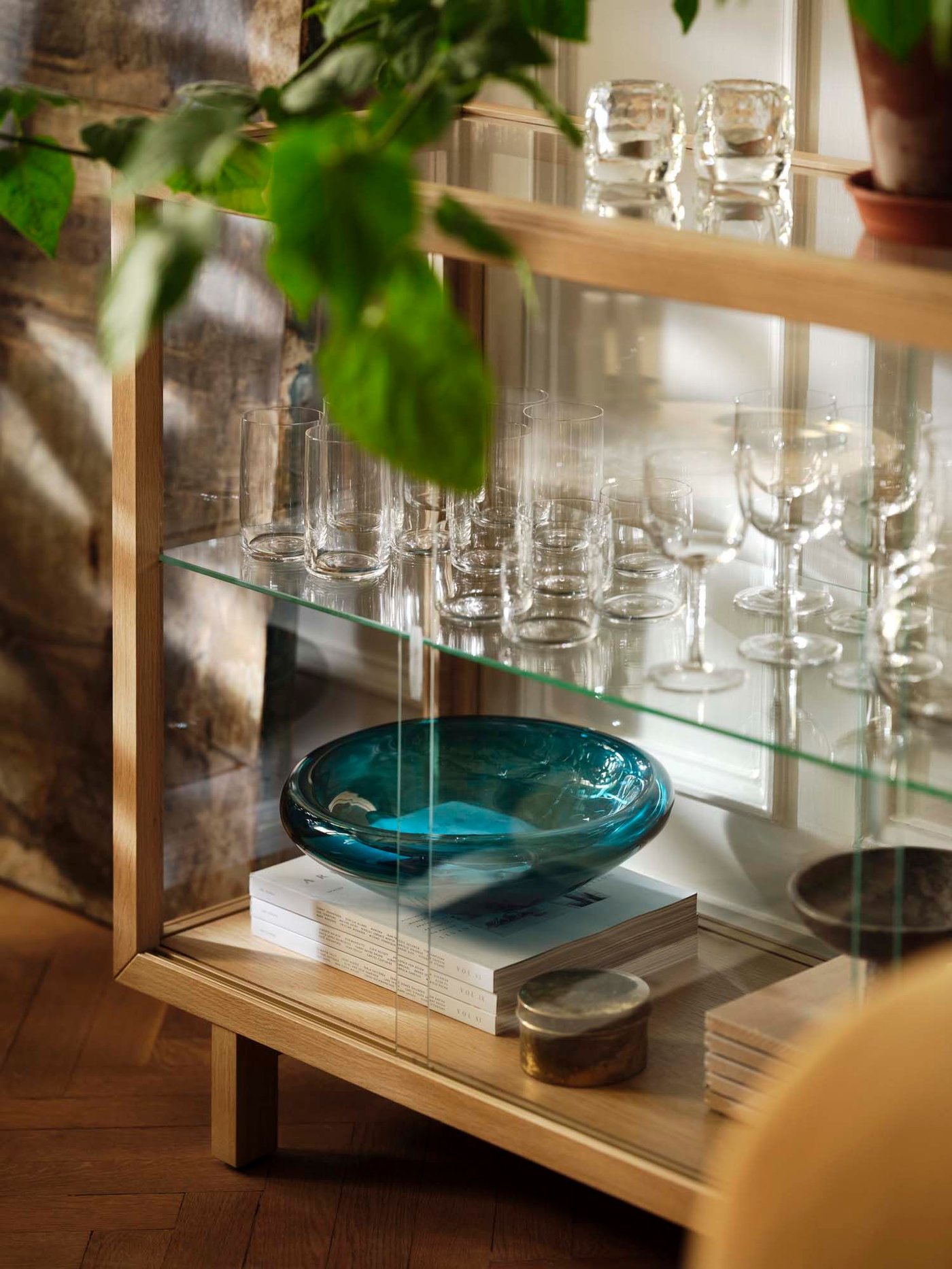 The corner of an oak veneer STOCKHOLM 2025 glass-door cabinet holding glassware from the same collection.