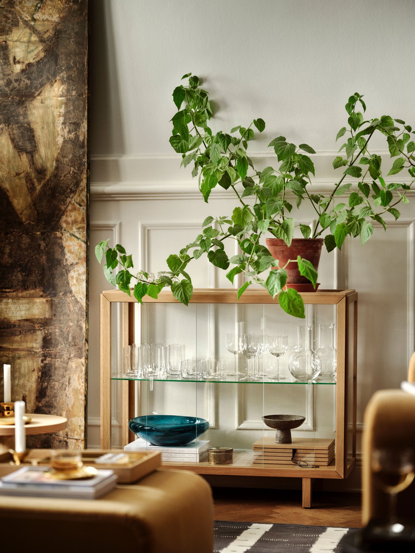 A cabinet with glass sides is standing in the back of the wall, with a pot and a green flower.