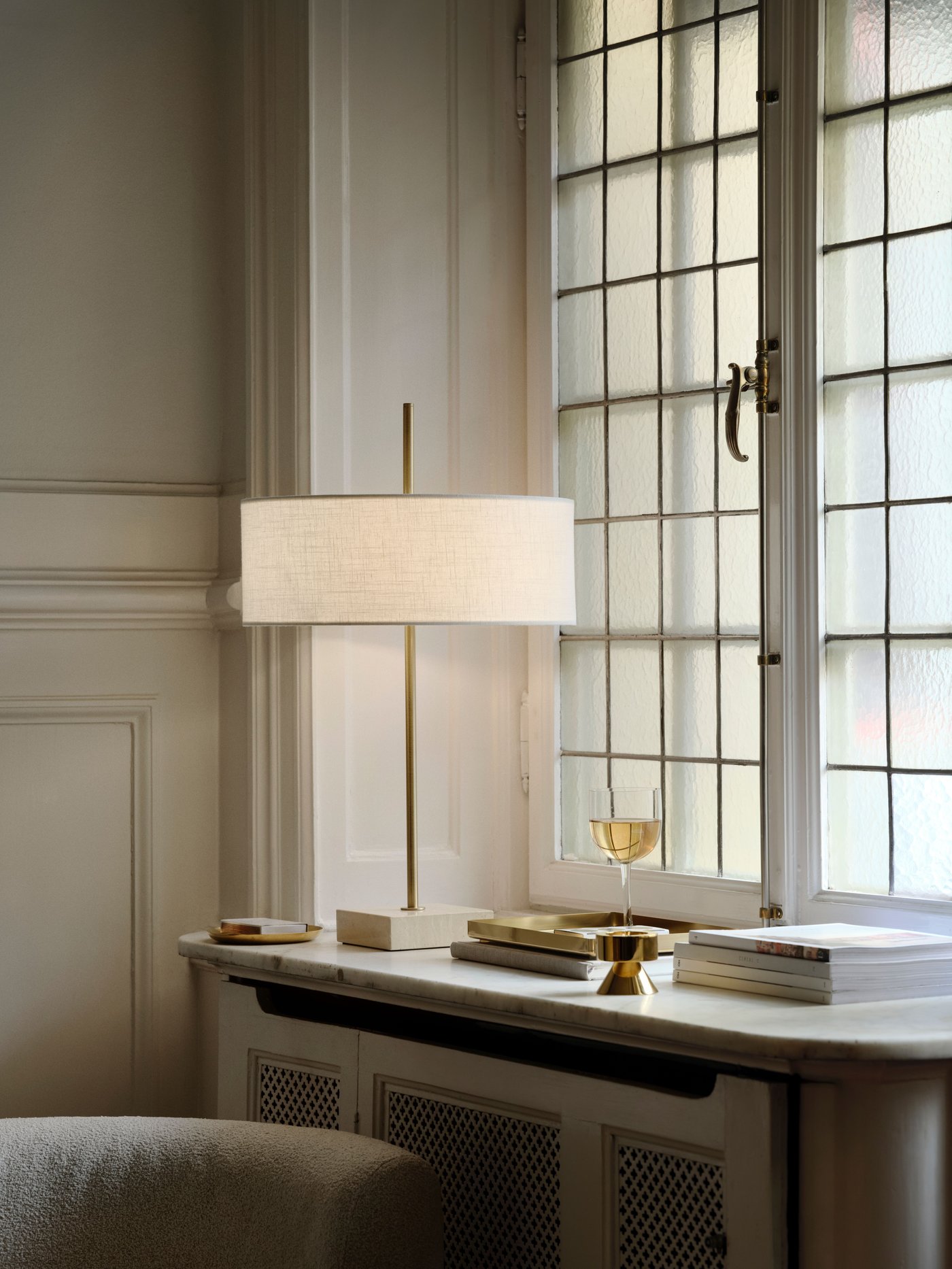 A STOCKHOLM 2025 table lamp with a white shade, on a windowsill, next to a window.