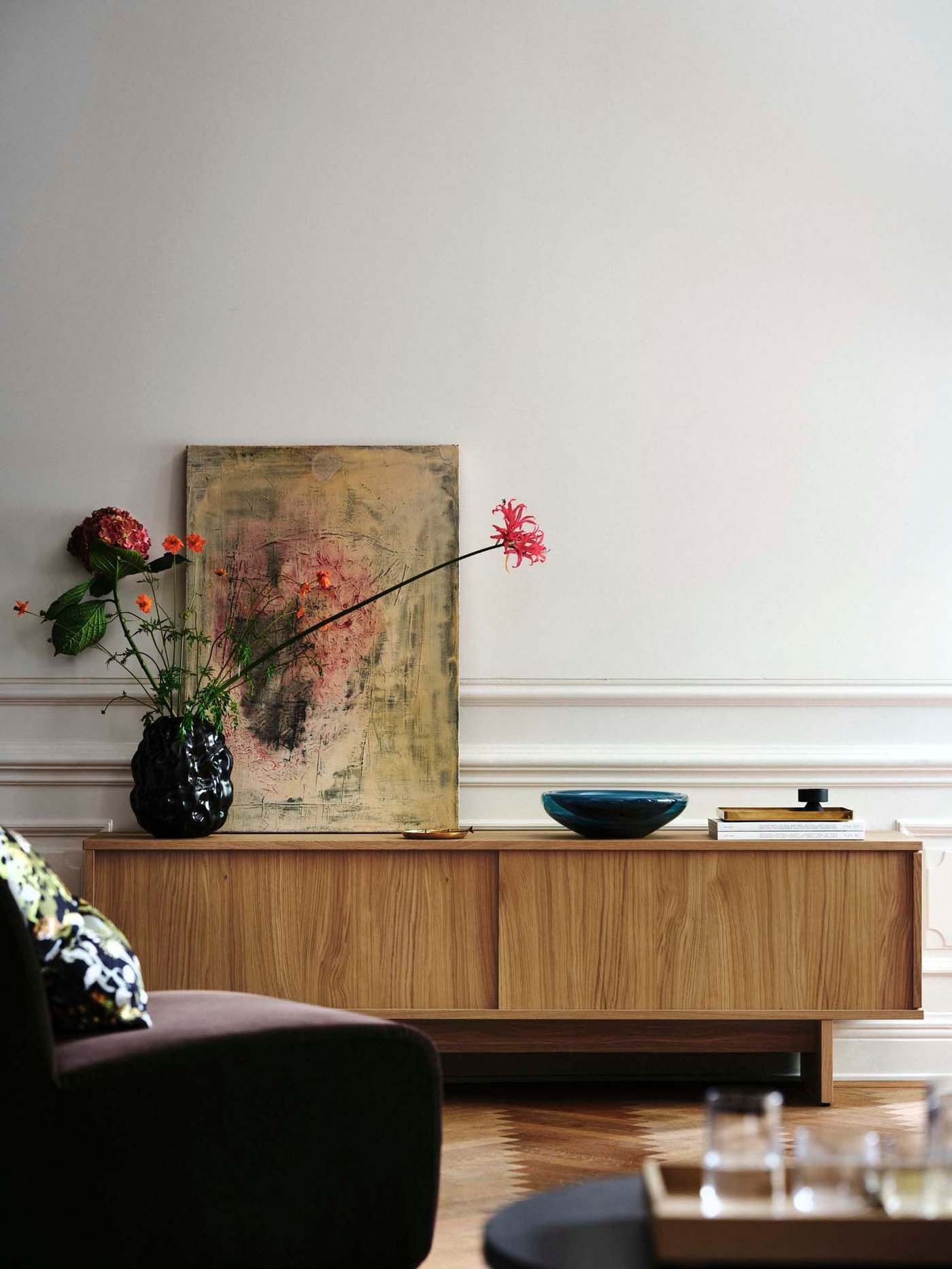 A wood storage unit with a vase, glassware and a painting on top.