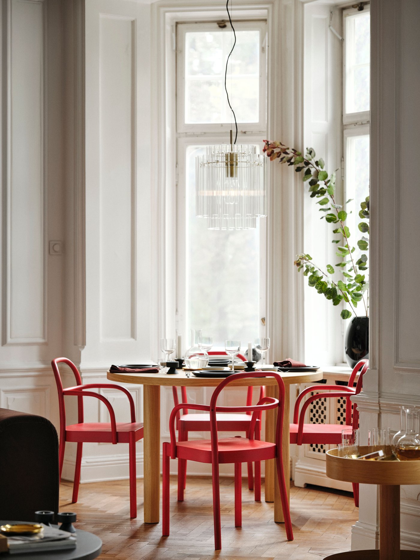 Round table with four red chairs in bentwood, with curved arches in back and armrest, in a bay window.