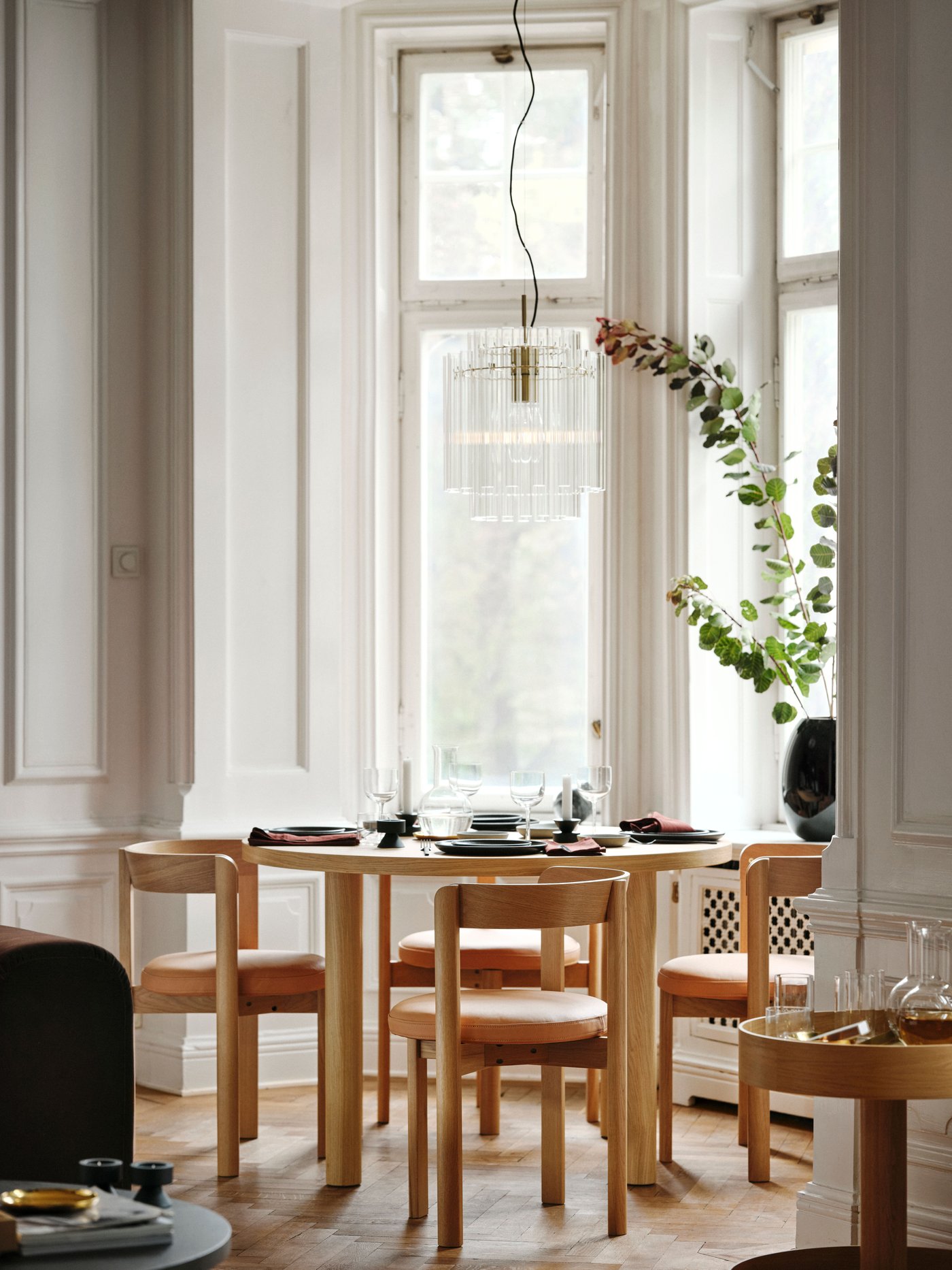Round table with four wooden chairs with curved back in a bay window. Wooden floors and soft natural light fill the apartment.
