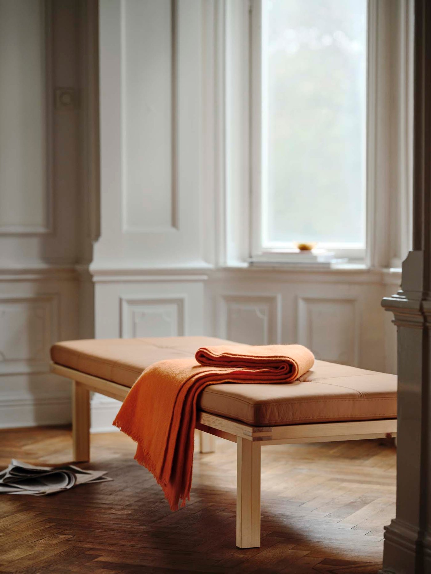 Pine daybed with an orange throw placed in a bay window, with large windows and decorations on the windowsill.