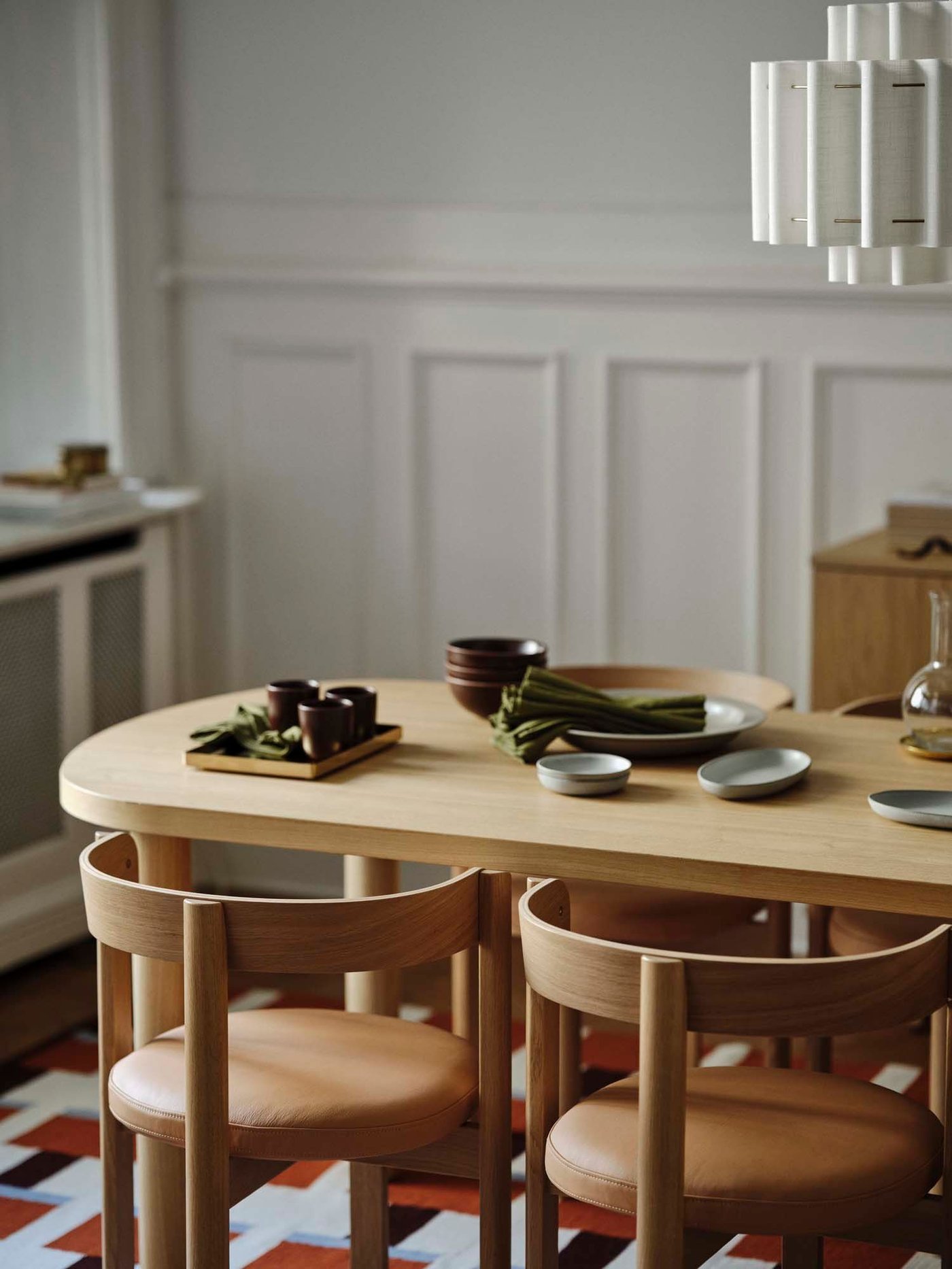 The corner of a dining room with a light wood table with tableware and wood and leather chairs.