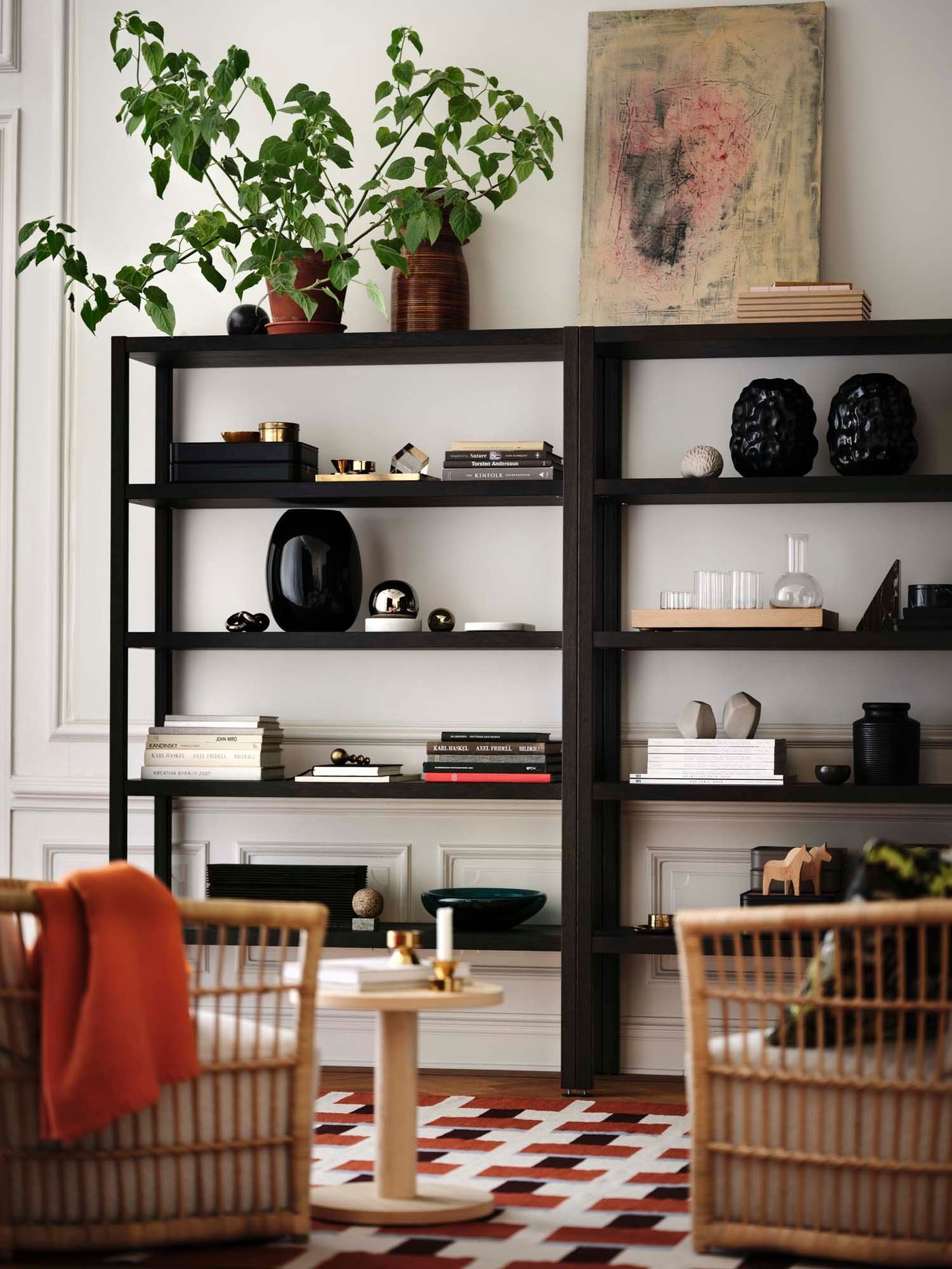 A dark oak veneer STOCKHOLM shelving unit filled with vases and ornaments, with rattan chairs in the foreground.