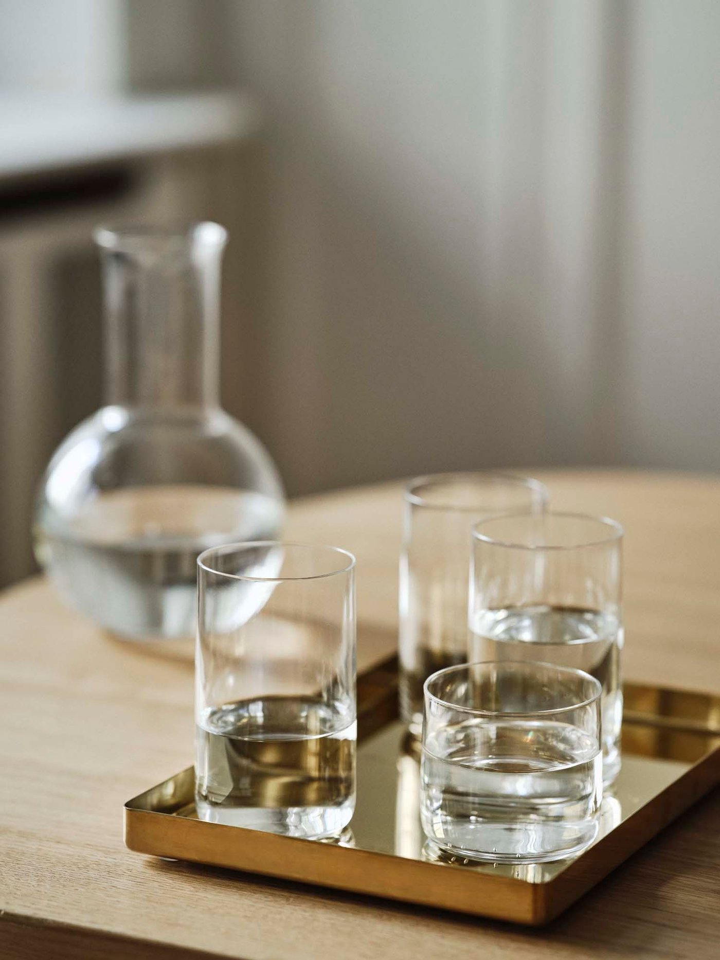 Glasses filled with water on a brass-coloured tray sit on a table, with a carafe in the background.