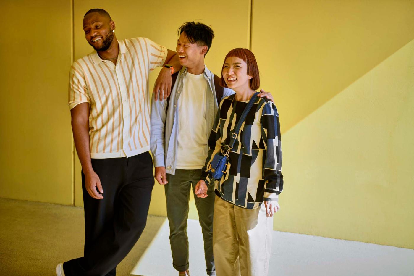 Three people laughing against a yellow backdrop.