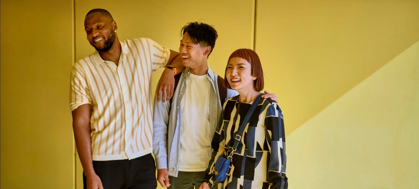 Three people laughing against a yellow backdrop.