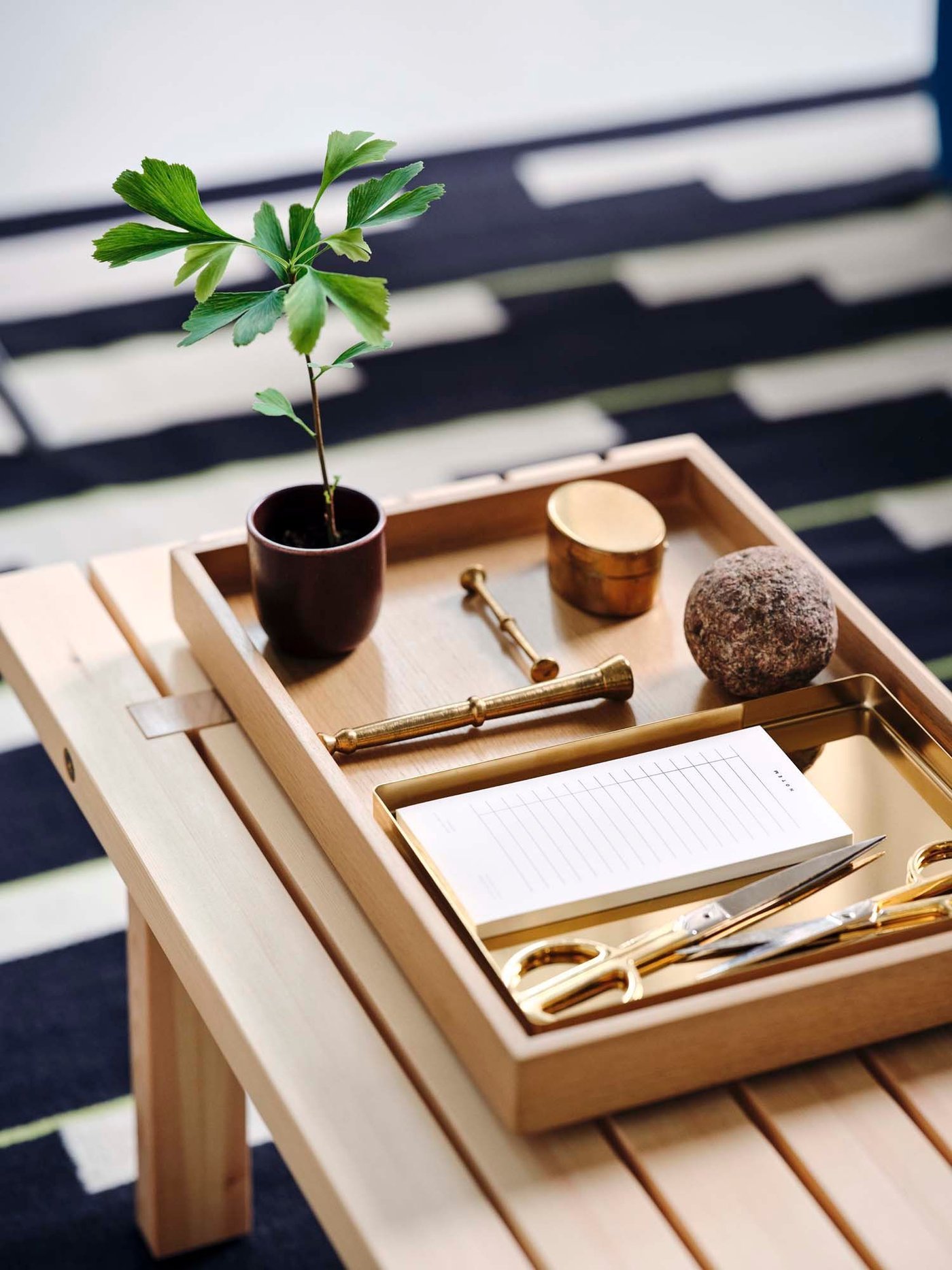 A wood tray filled with objects on the light wood bench from the STOCKHOLM collection.