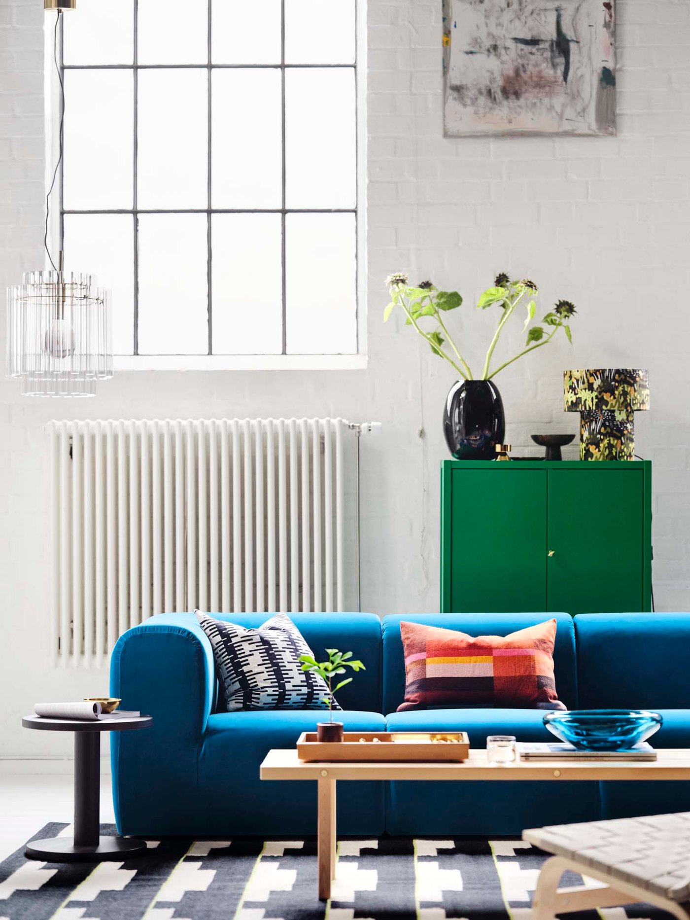 Front view of blue-turquoise sofa in an industrial room with large ceiling-high windows.