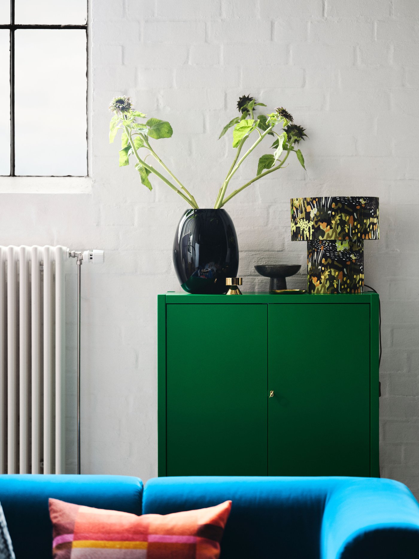 A bright green storage unit with vases on top, behind the top of a blue velvet sofa.