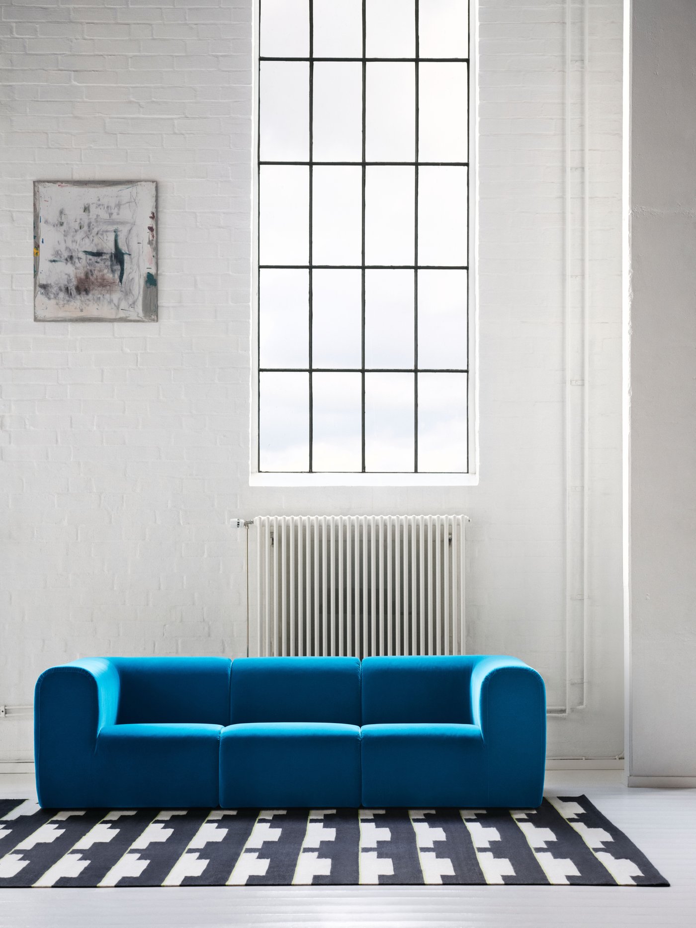 Turquoise sofa in an industrial room with tall windows and high ceiling.