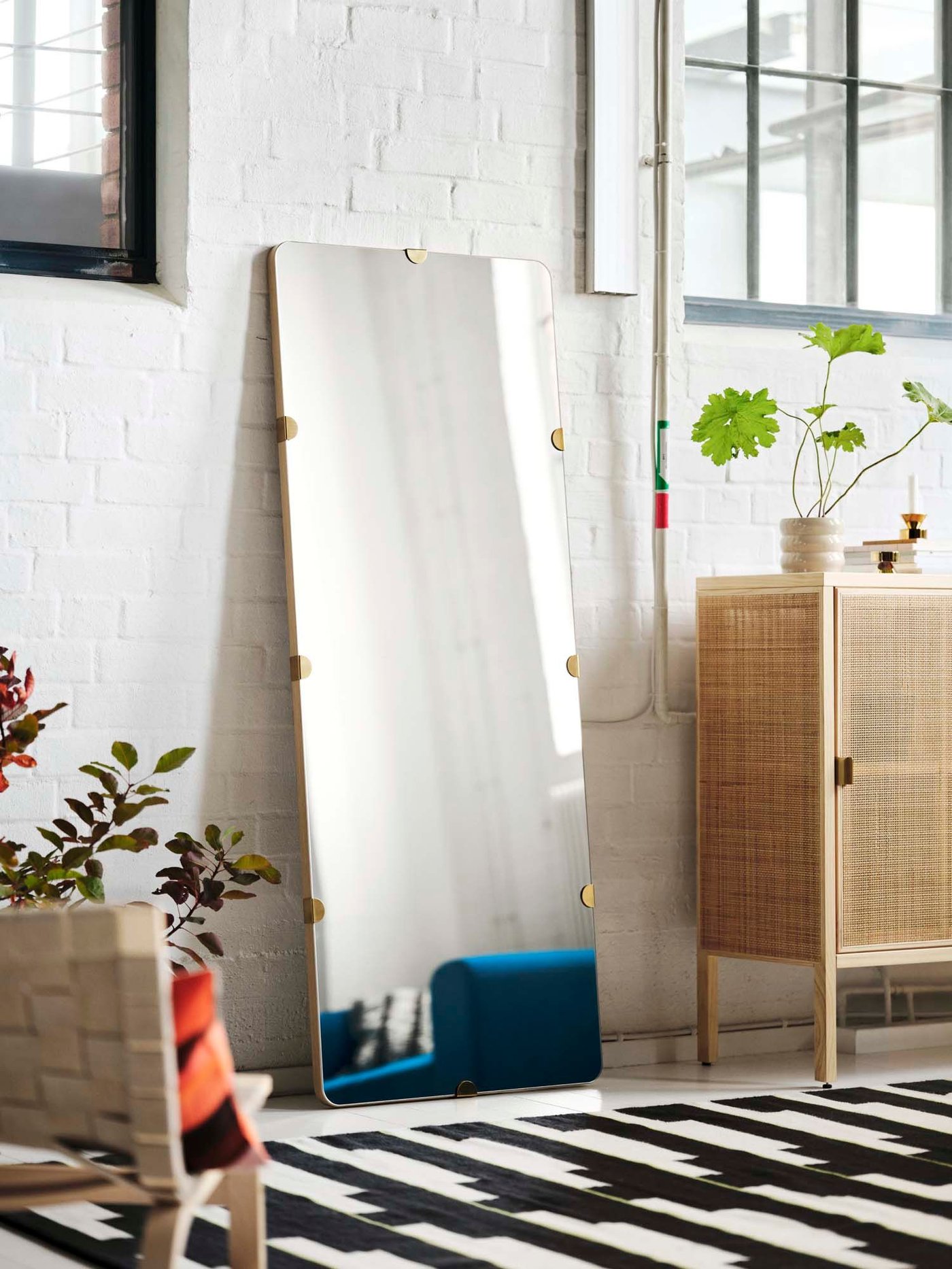 A mirror and rattan cabinet against the wall in a white room.