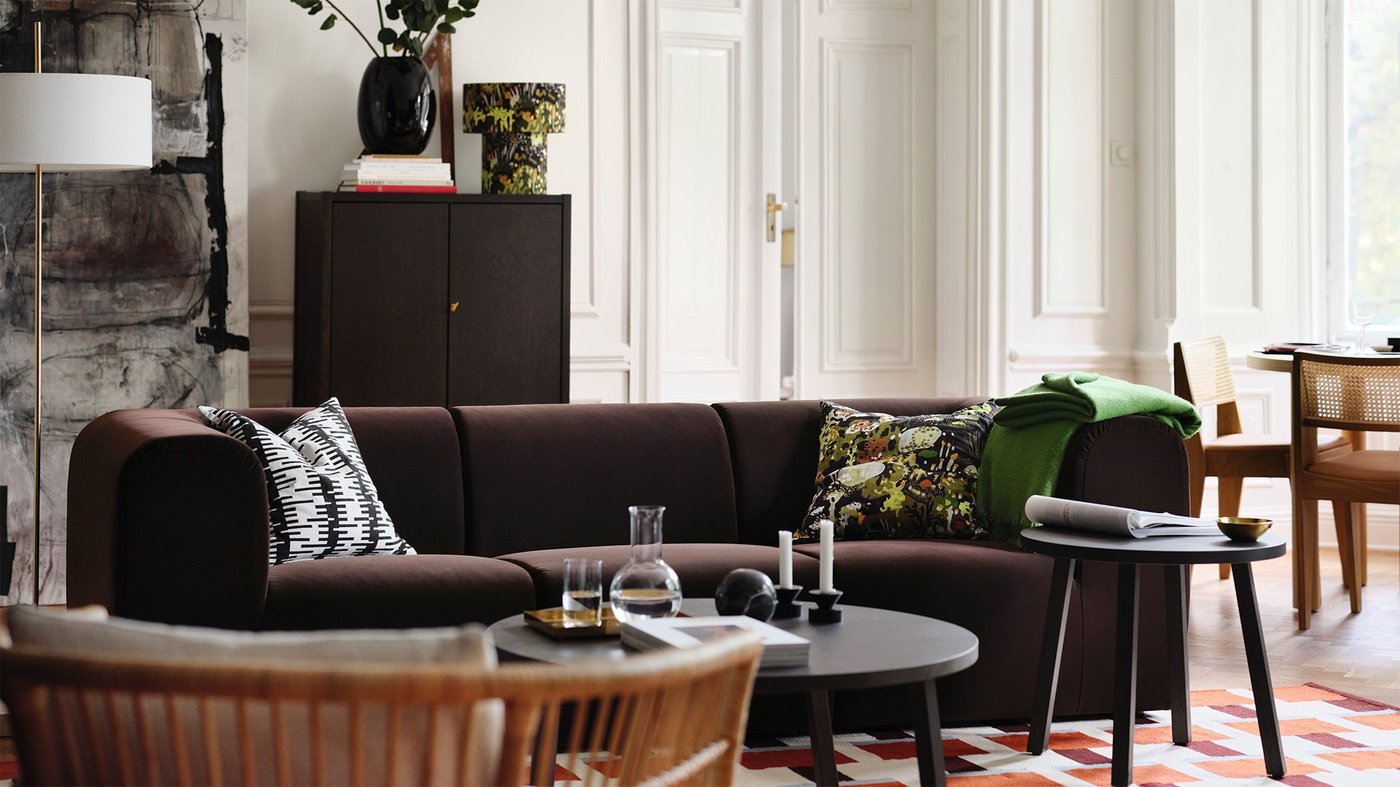 A white living room with a dark brown sofa and dark storage unit in the background.