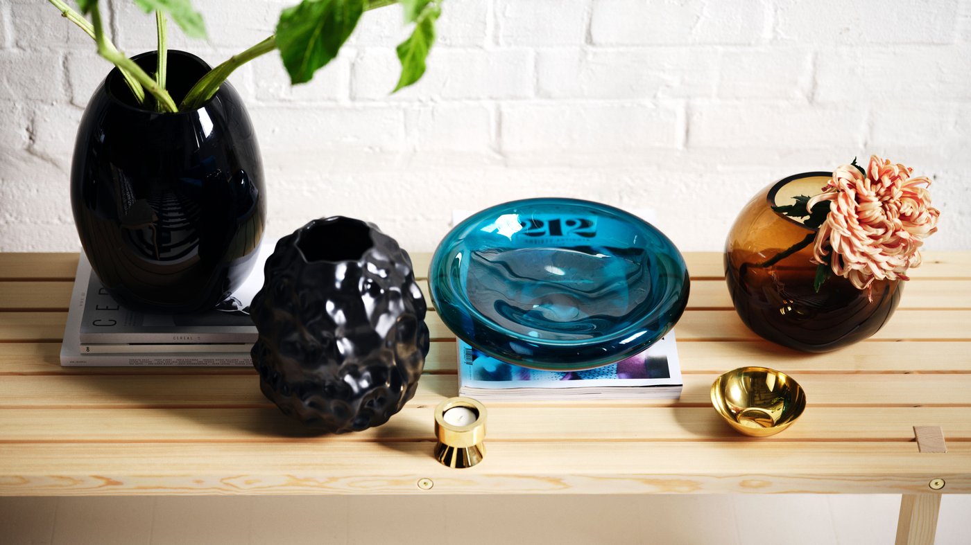 Four vases in black, blue, and light brown on a solid pine bench. A mix of mouth-blown and ceramic pieces, each with distinct character.