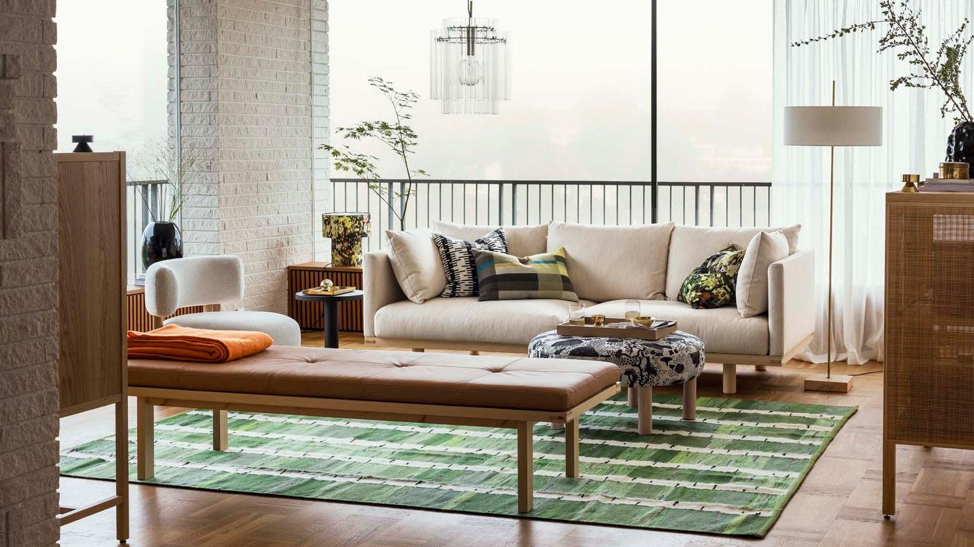 A living room with a sofa and daybed on a rug, in front of large windows.