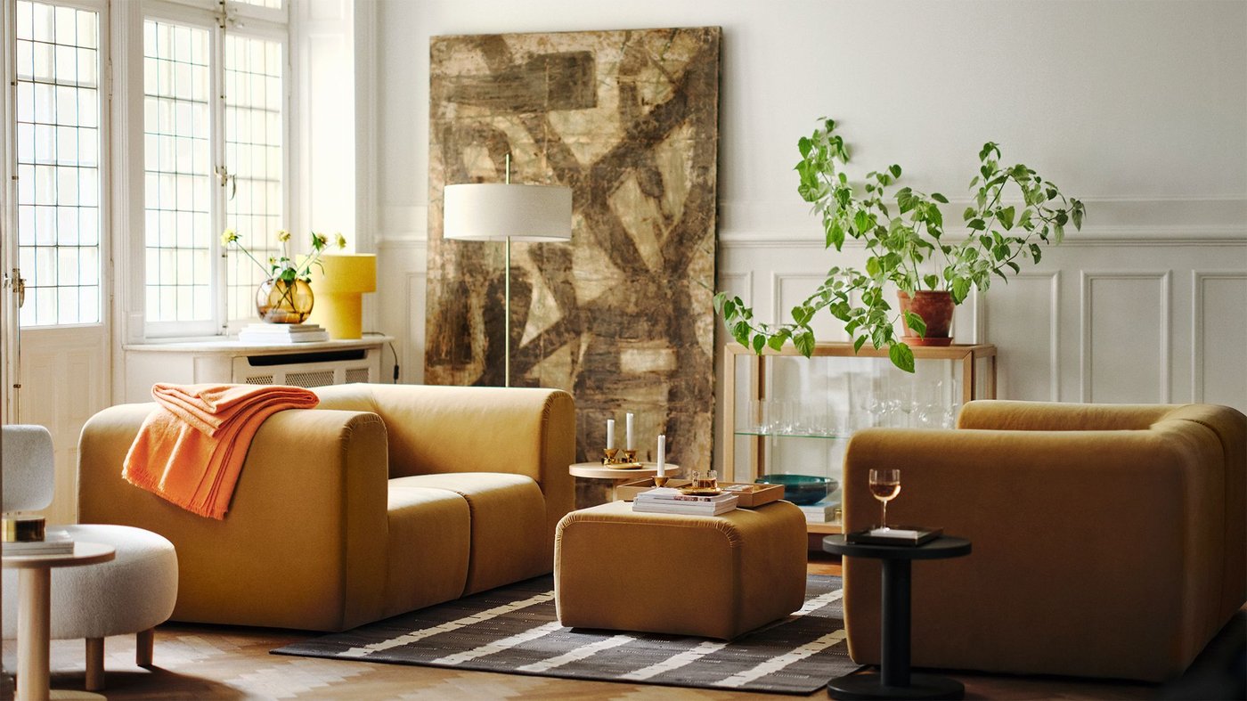 A living room filled with furniture from the STOCKHOLM 2025 collection, dominated by two yellow sofas and a footstool.