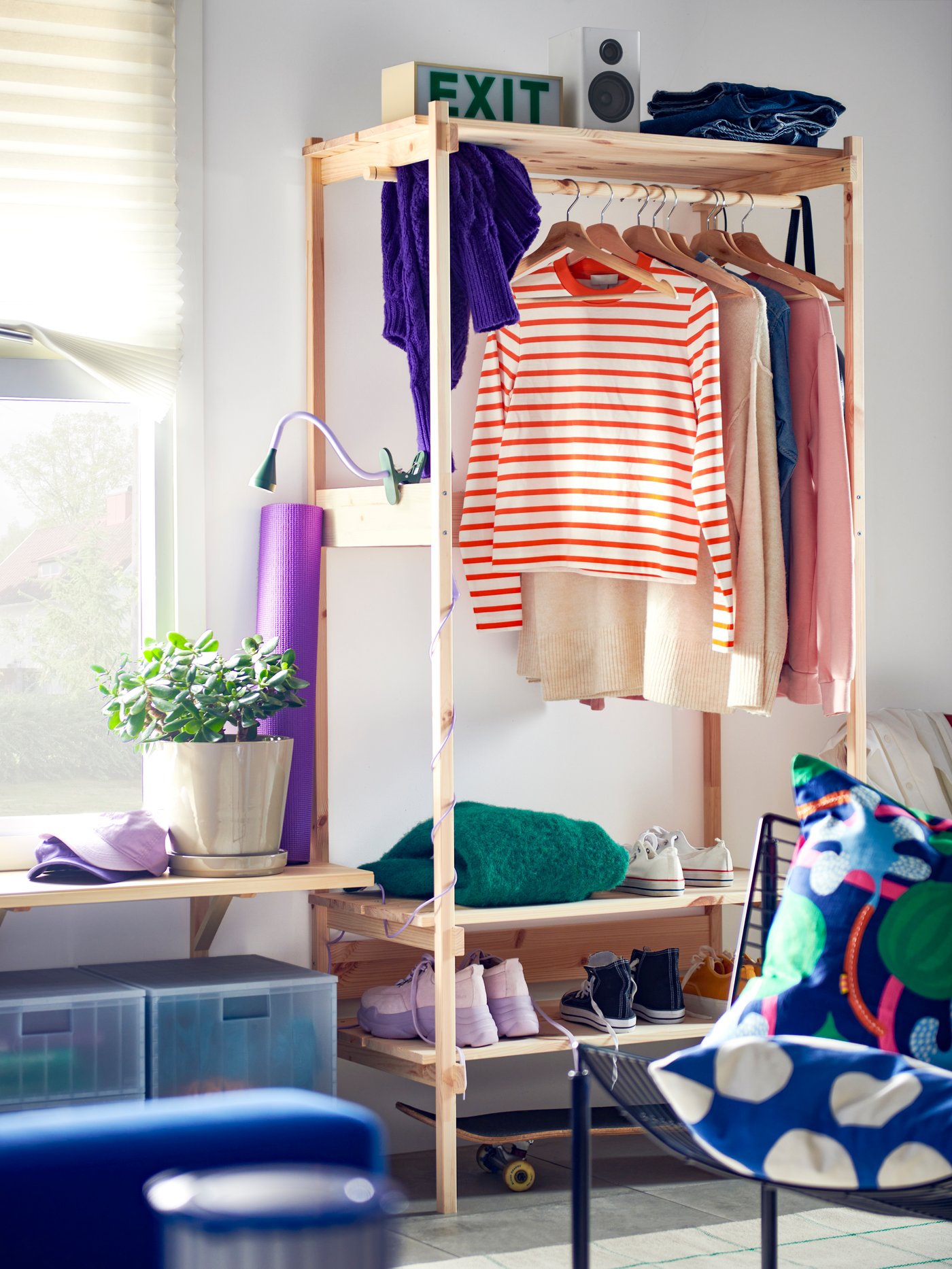 The KRONÖREN open wardrobe in pine in a bedroom setting, holding hanging clothes, shoes and other accessories.