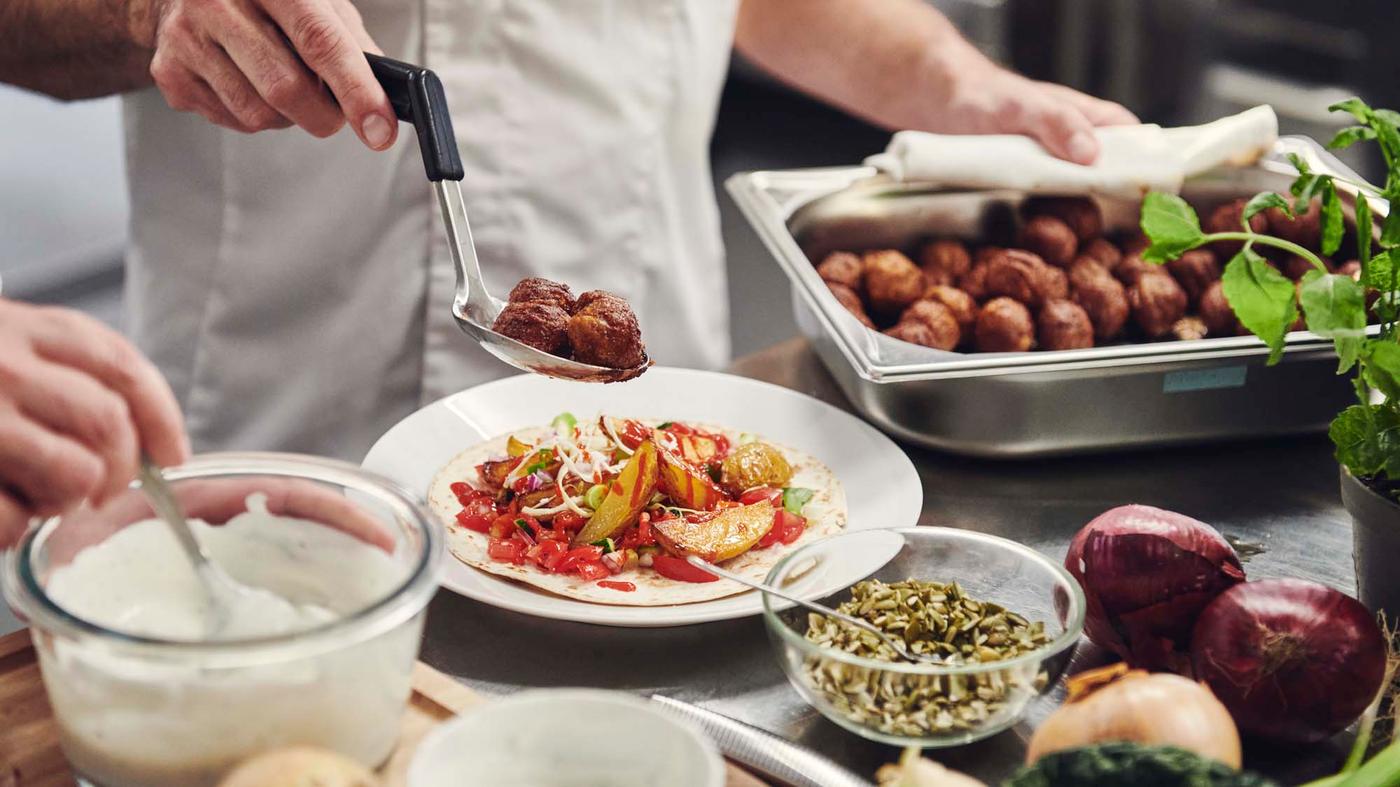 A chef spooning plant balls onto crispy potatoes and pancakes on a plate.