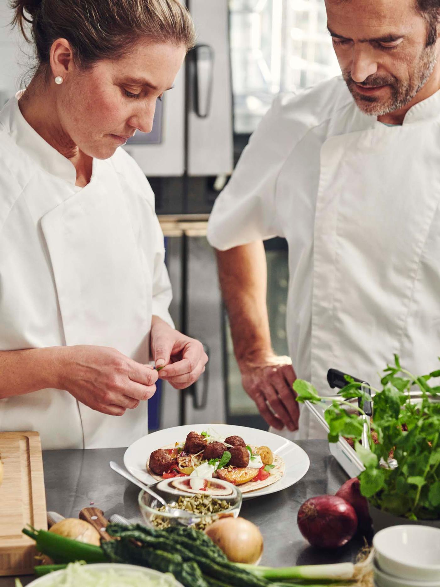 Two people creating a dish of plant-based balls with crispy potato pancakes.