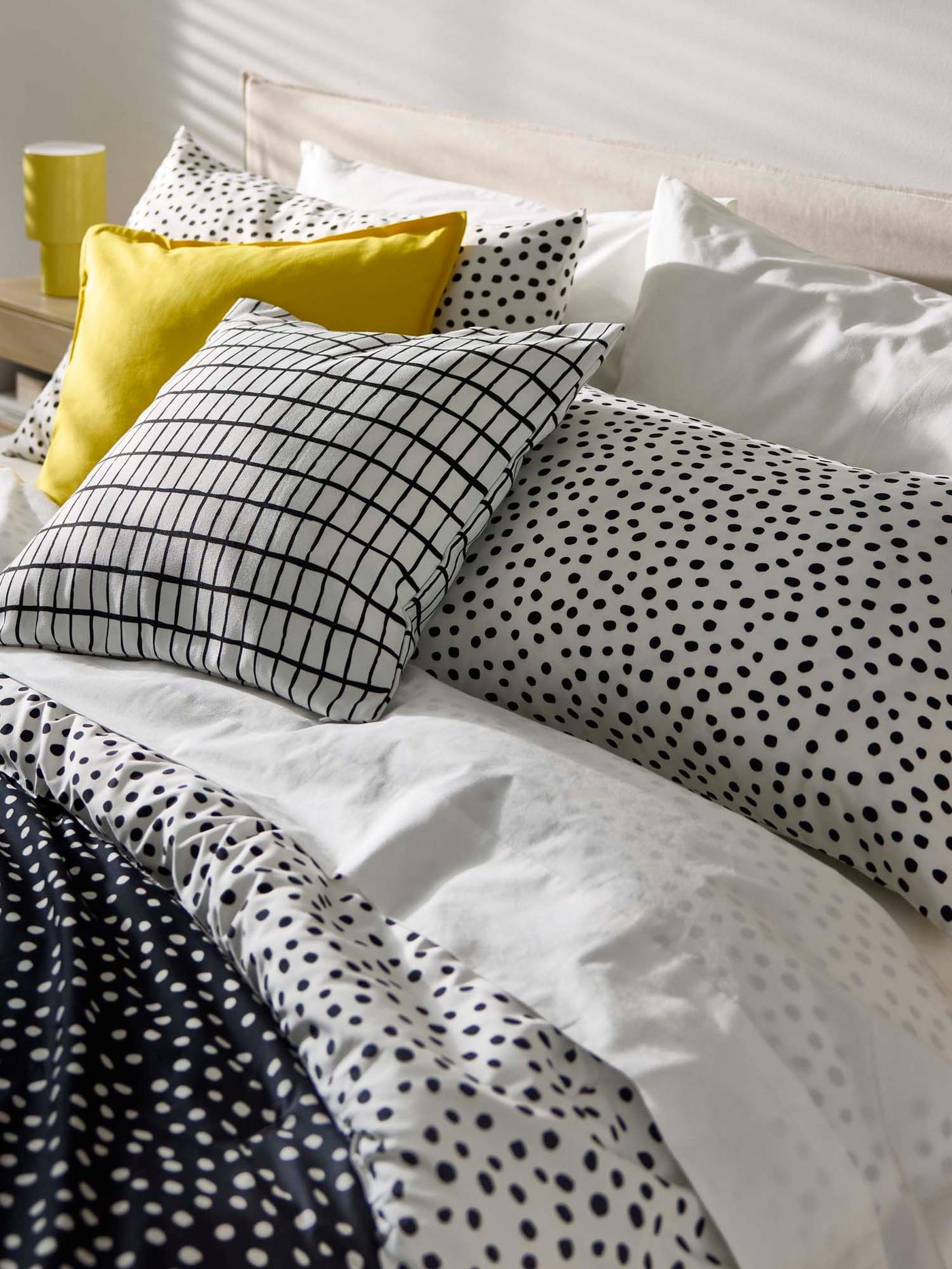 Solid yellow and black and white pillows in mixed patterns sit on a cosy looking bed.