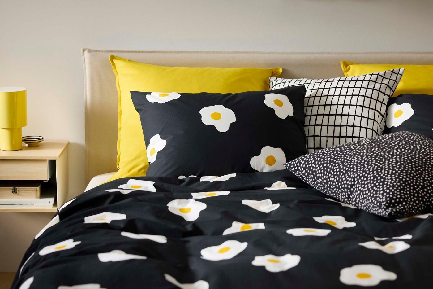 A bed with black patterned bed linen, with yellow pillows.