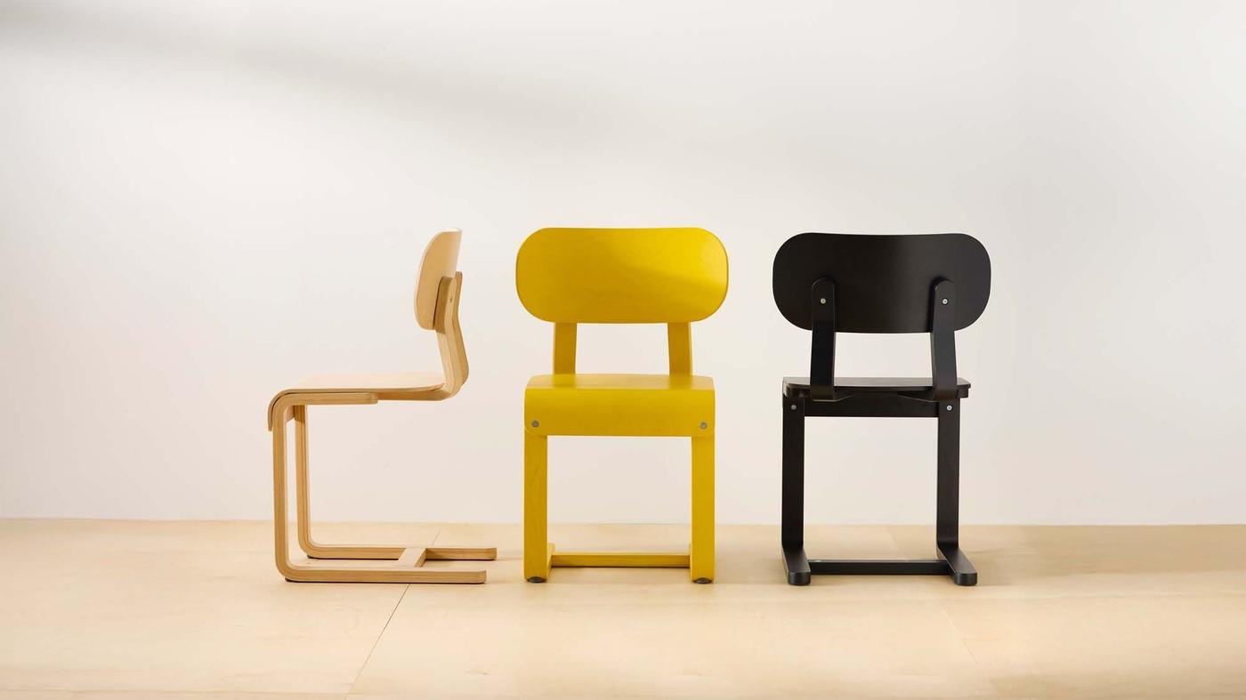 Three LYCKAN chairs in natural, yellow and black birch veneer on a beige floor against a white wall.