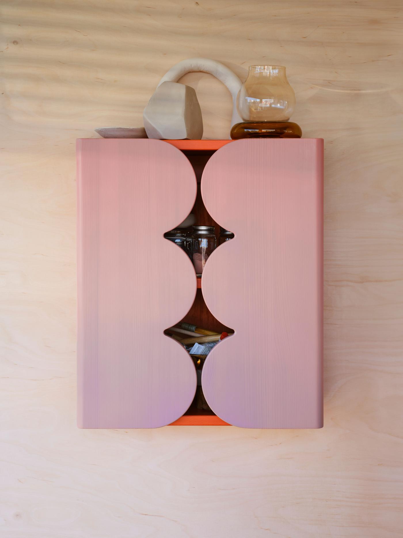 A pink cabinet hangs on a wood wall.