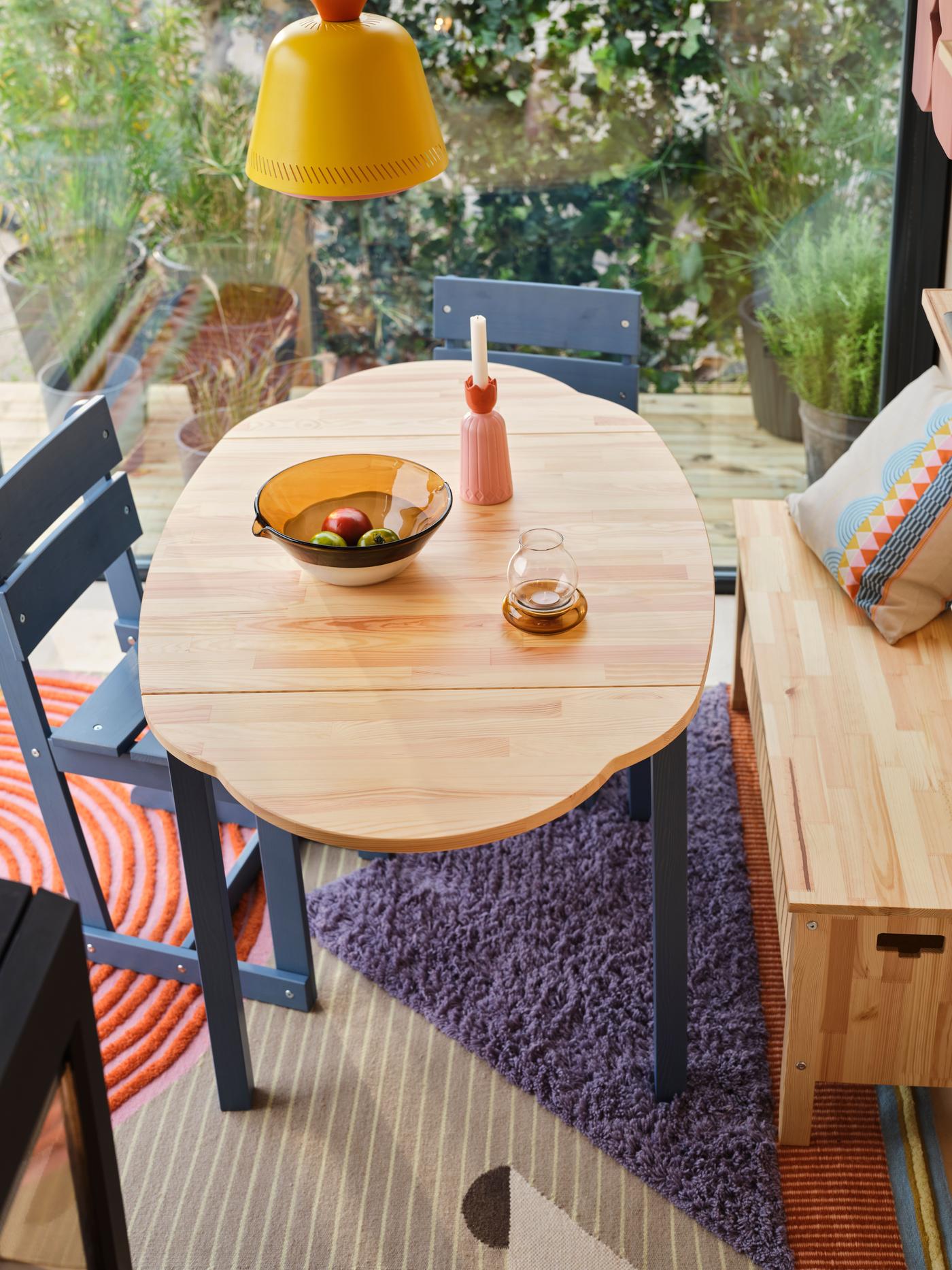 An aerial view of a wood dining table and blue chairs, with a yellow lamp above.