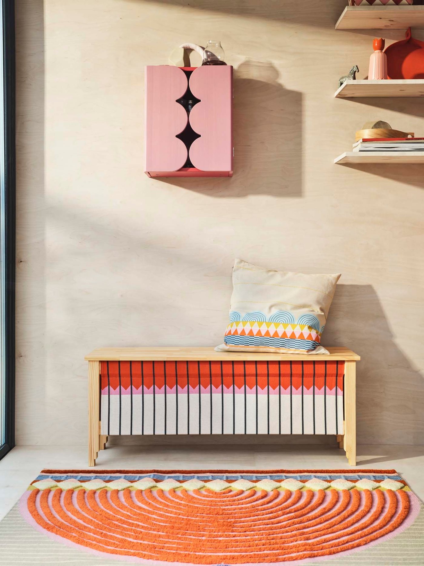 A pink cupboard hangs on a wood wall above a colourful storage bench from the OMMJÄNGE collection.