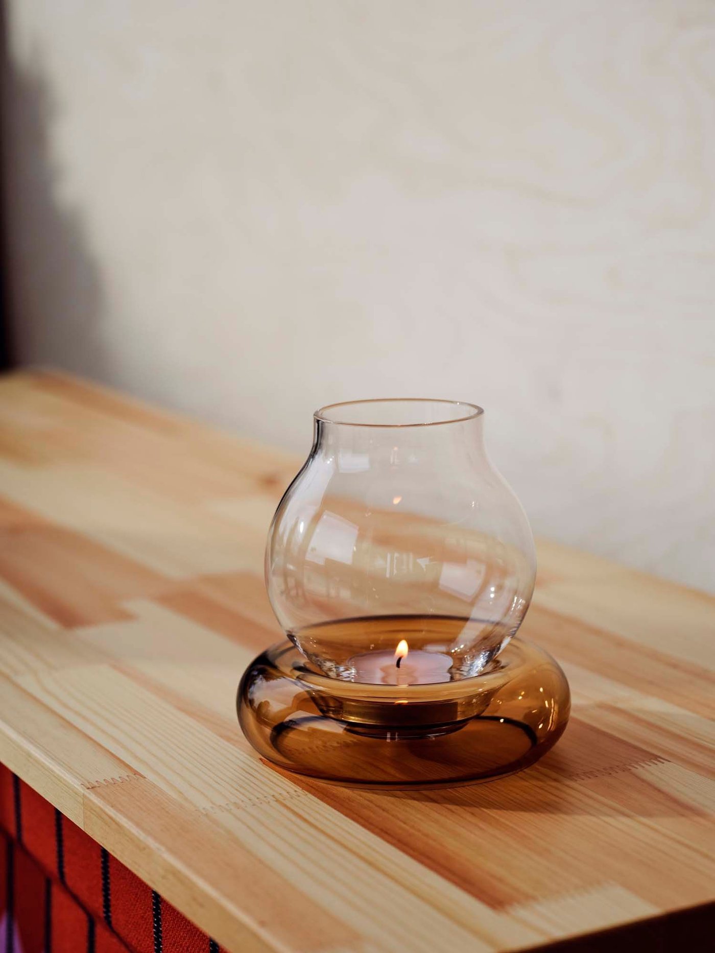 A glass OMMJÄNGE tealight holder on a wooden shelf.