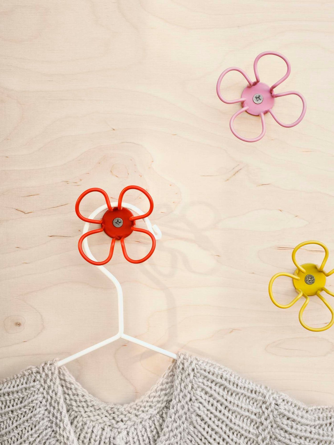 Flower-shaped metal OMMJÄNGE hooks on a wood wall with a top hanging on a hanger.