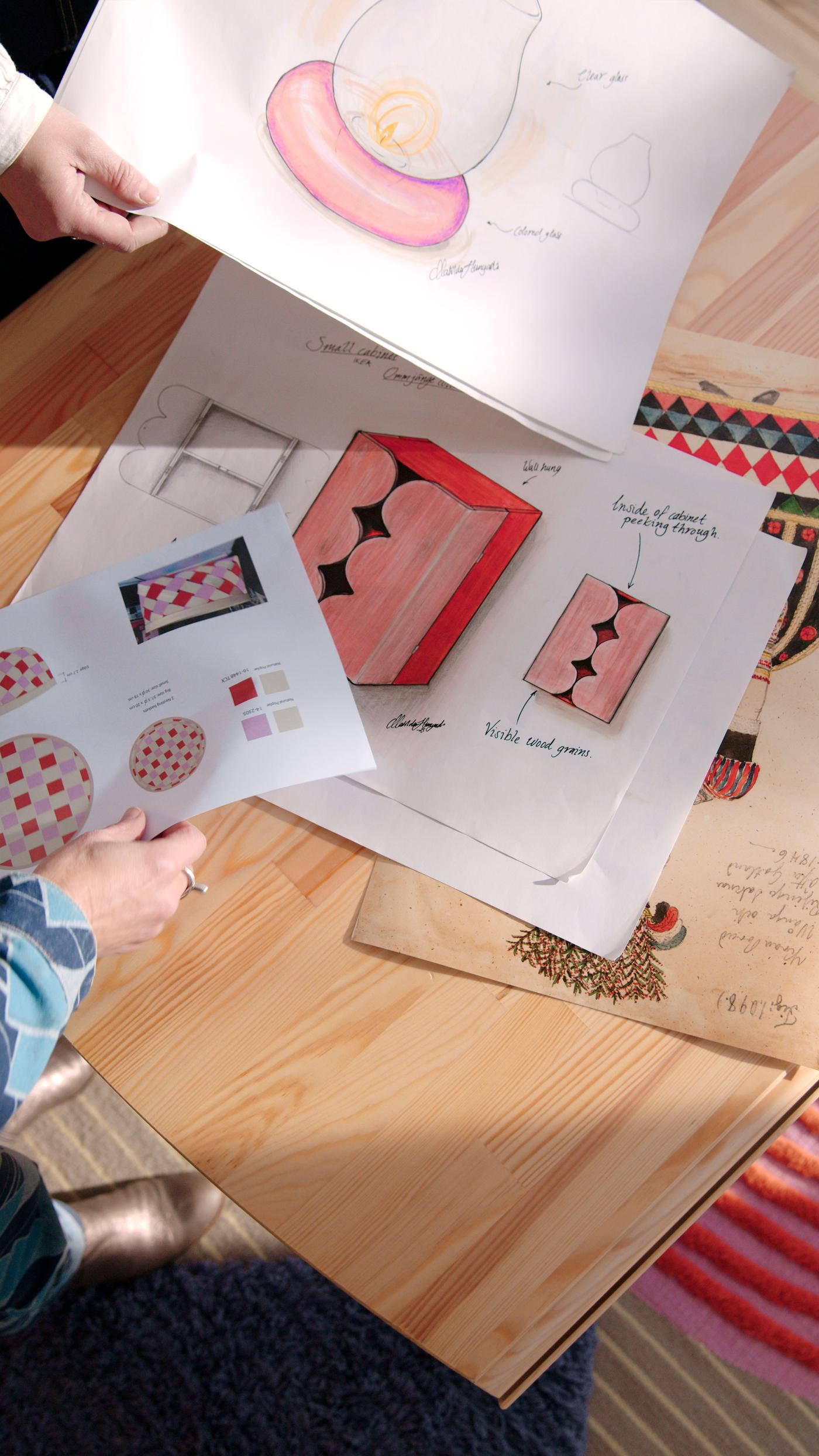 An aerial view of hands holding sketches of products from the OMMJÄNGE collection, over a wood table.