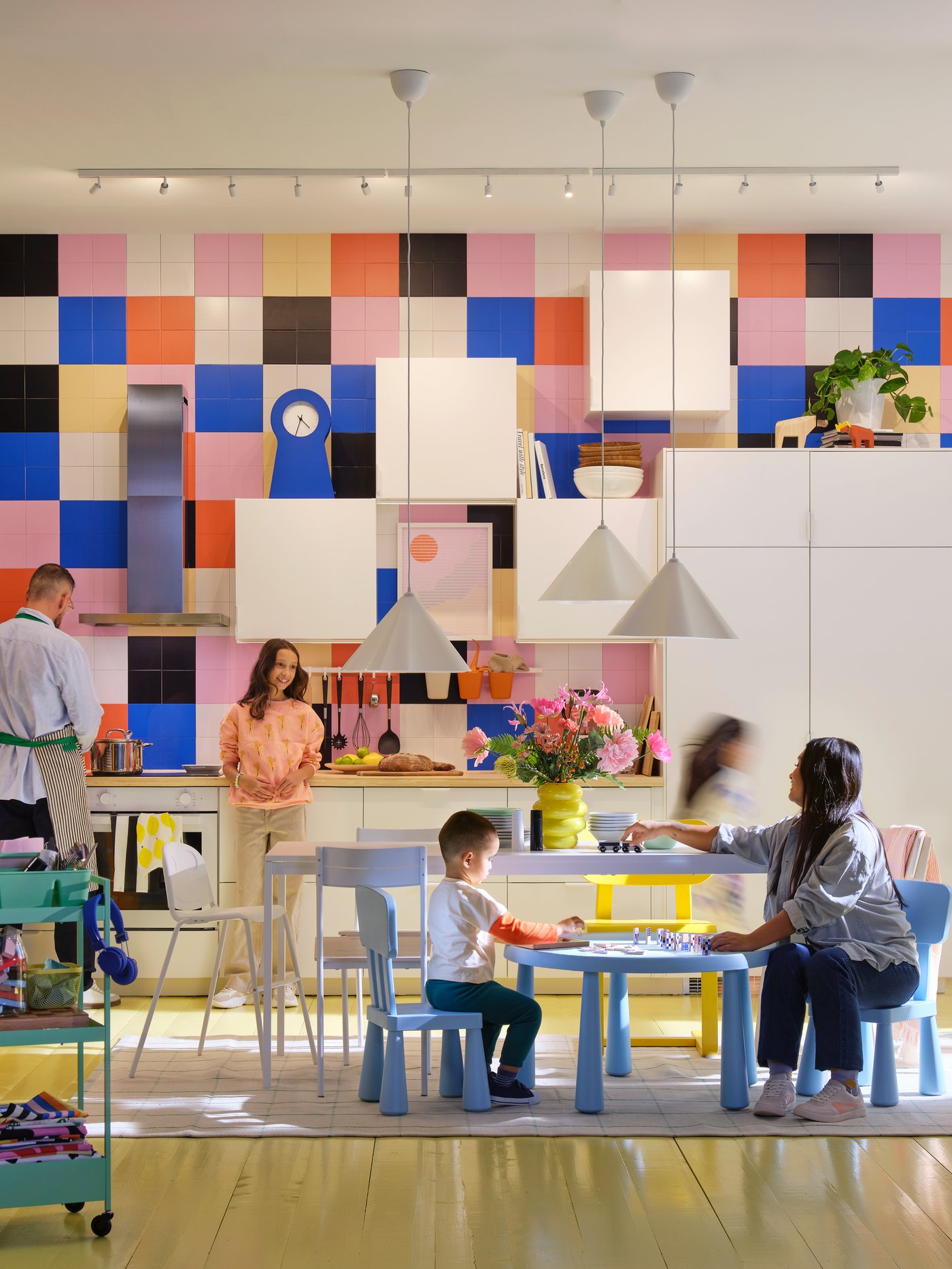 A family of five hanging out in a kitchen with a multi-coloured graphical wall, white cabinets and a yellow floor.