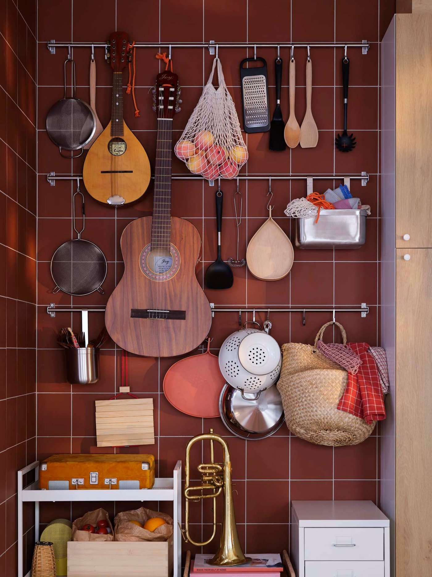 Cooking utensils and guitars hang from metal KUNGSFORS rails and hooks against burnt orange tiles.