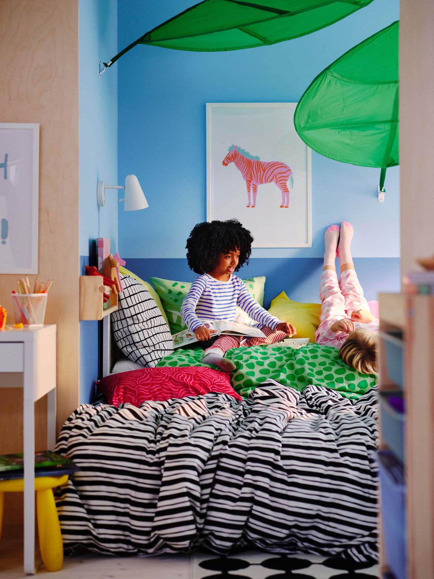 Two children sitting on a bed with vibrant coloured bed linen.