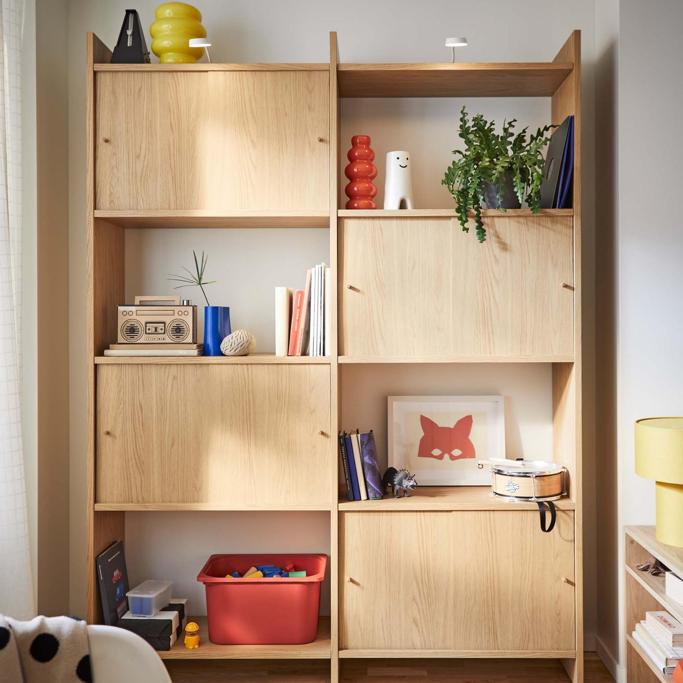 A LÅDMAKARE storage system with four cupboards, interspersed with colourful, decorative objects, such a drawings and vases.