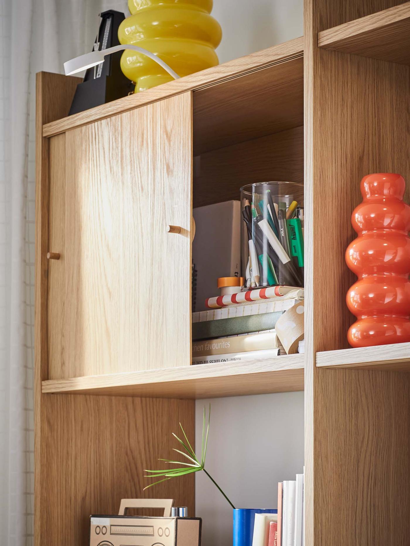 A close-up of a slightly open cupboard in the LÅDMAKARE storage system, revealing books and pens.