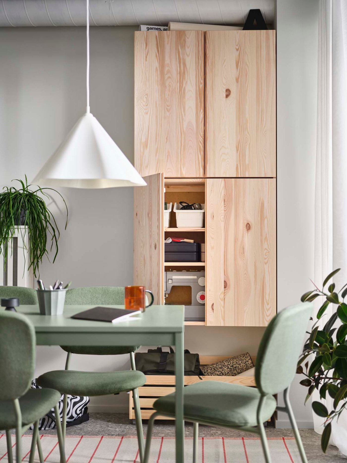 A soft, natural coloured dining room with a green dining room set, wood cupboards and plants.