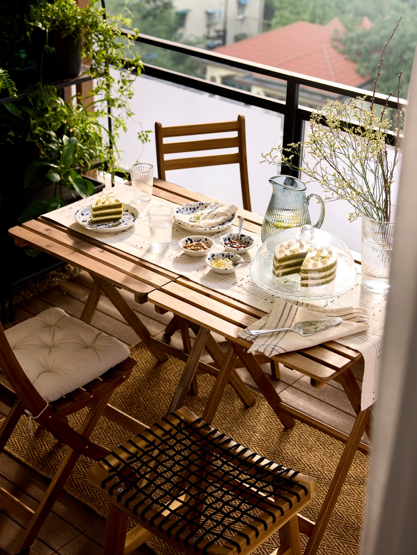 An aerial view of a small balcony with a wooden table and four chairs. The table is set with cake and a jug of water.