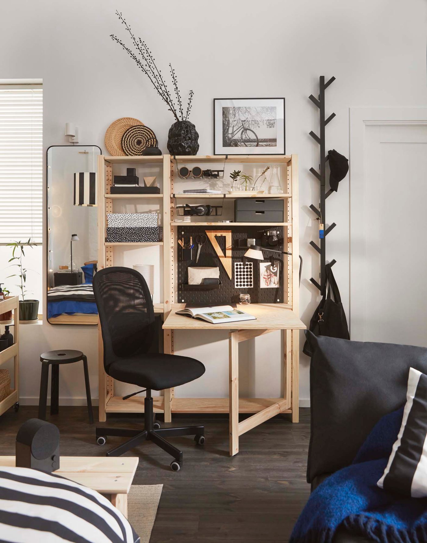 A wooden IVAR shelf filled and table filled with objects in a light bedroom.